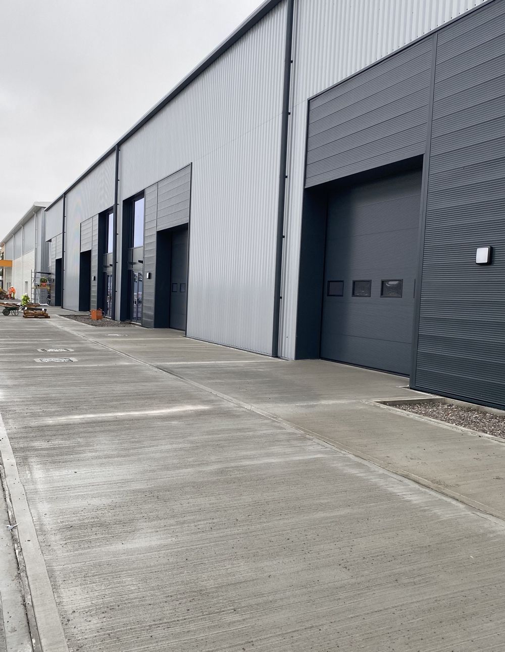 Exterior of a modern industrial building with multiple gray roller doors and a concrete apron.