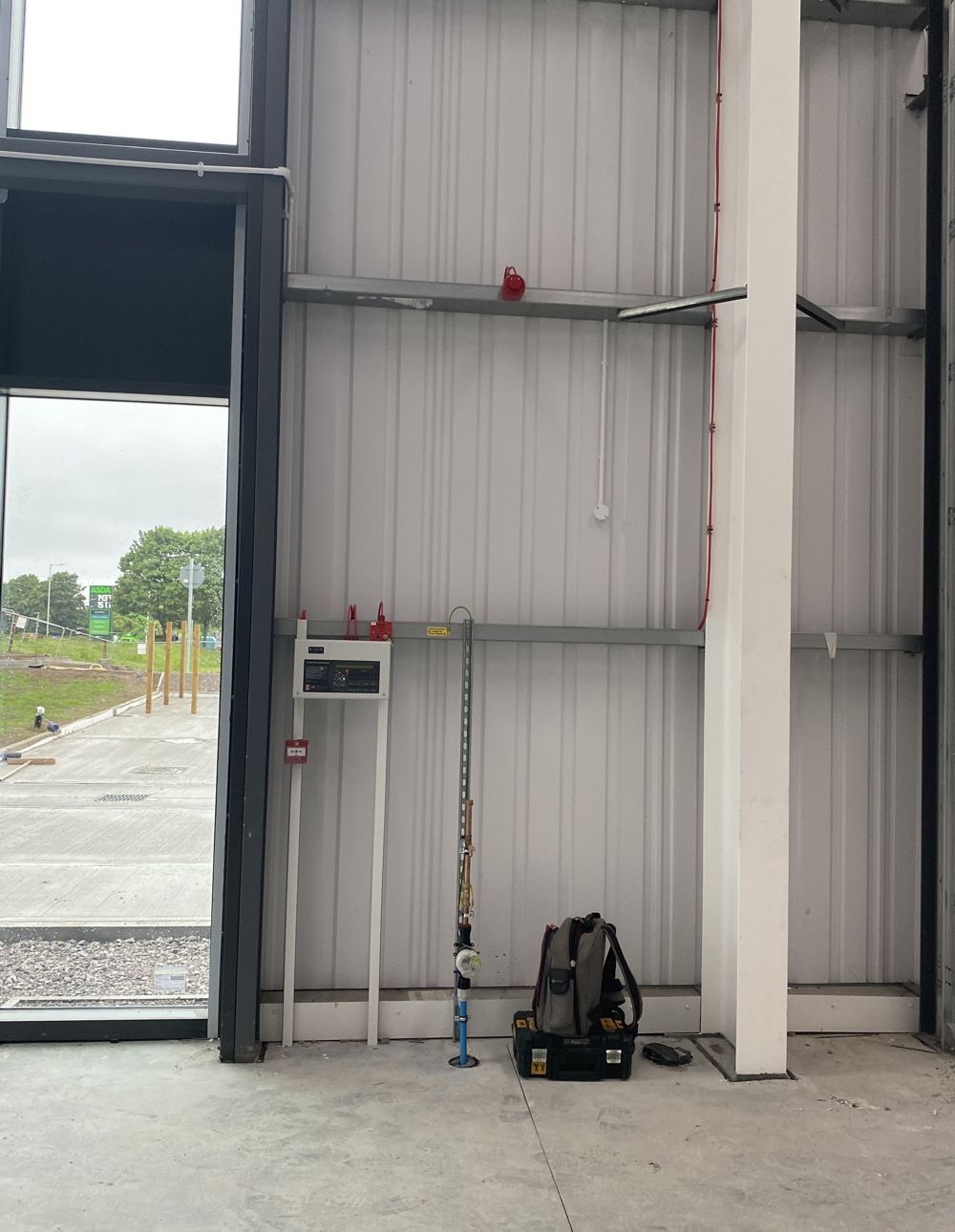 Interior of a building under construction with exposed metal walls, tools, and an open door framing an exterior view.