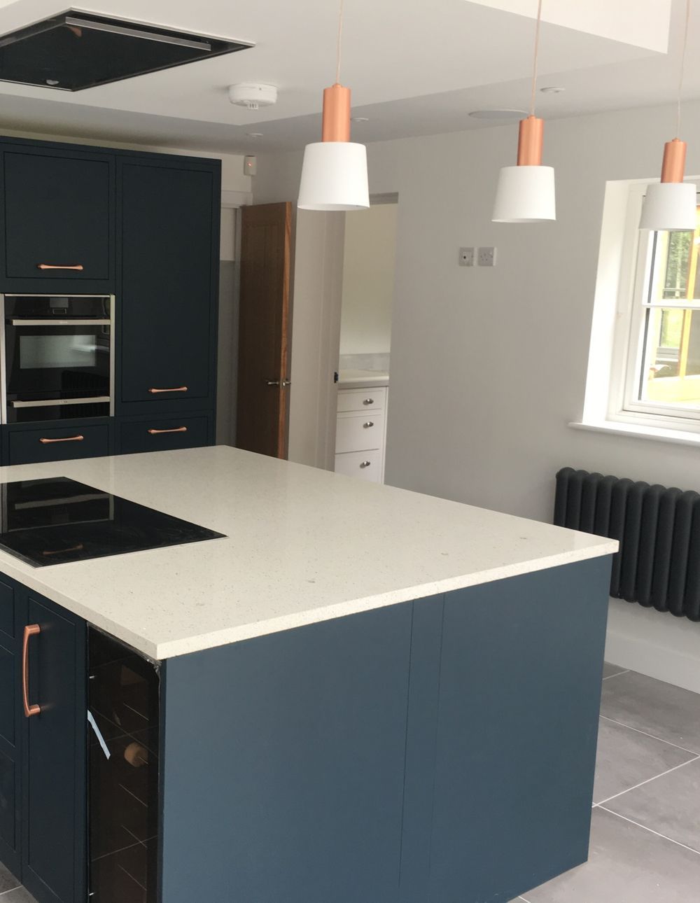 Modern navy blue kitchen with white countertops, island, and pendant lights.