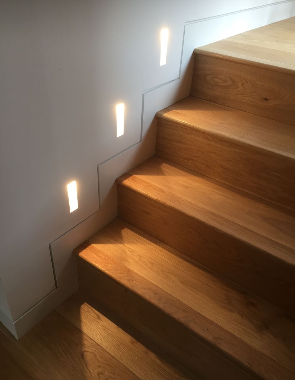 Wooden stairs with wall-mounted lights illuminating the steps.
