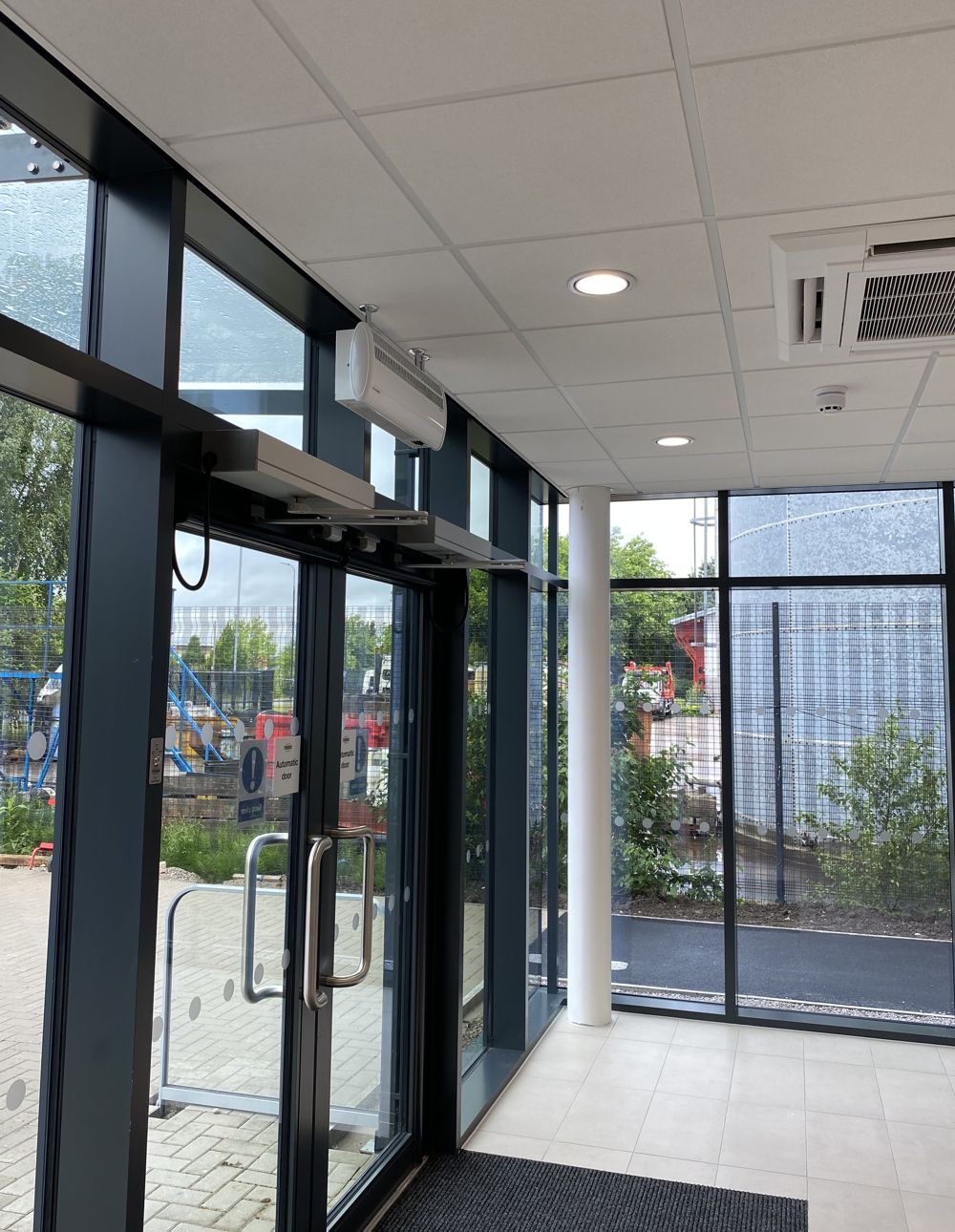 Automatic door in a glass doorway, with push bars and overhead closer.  Interior hallway with tiled ceiling.
