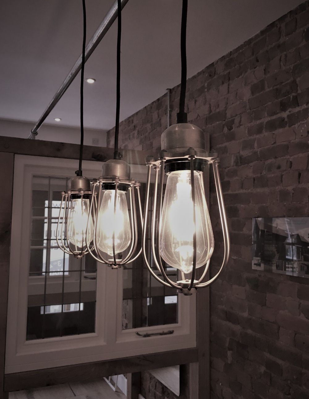 Three industrial pendant lights hanging near a brick wall and a window.