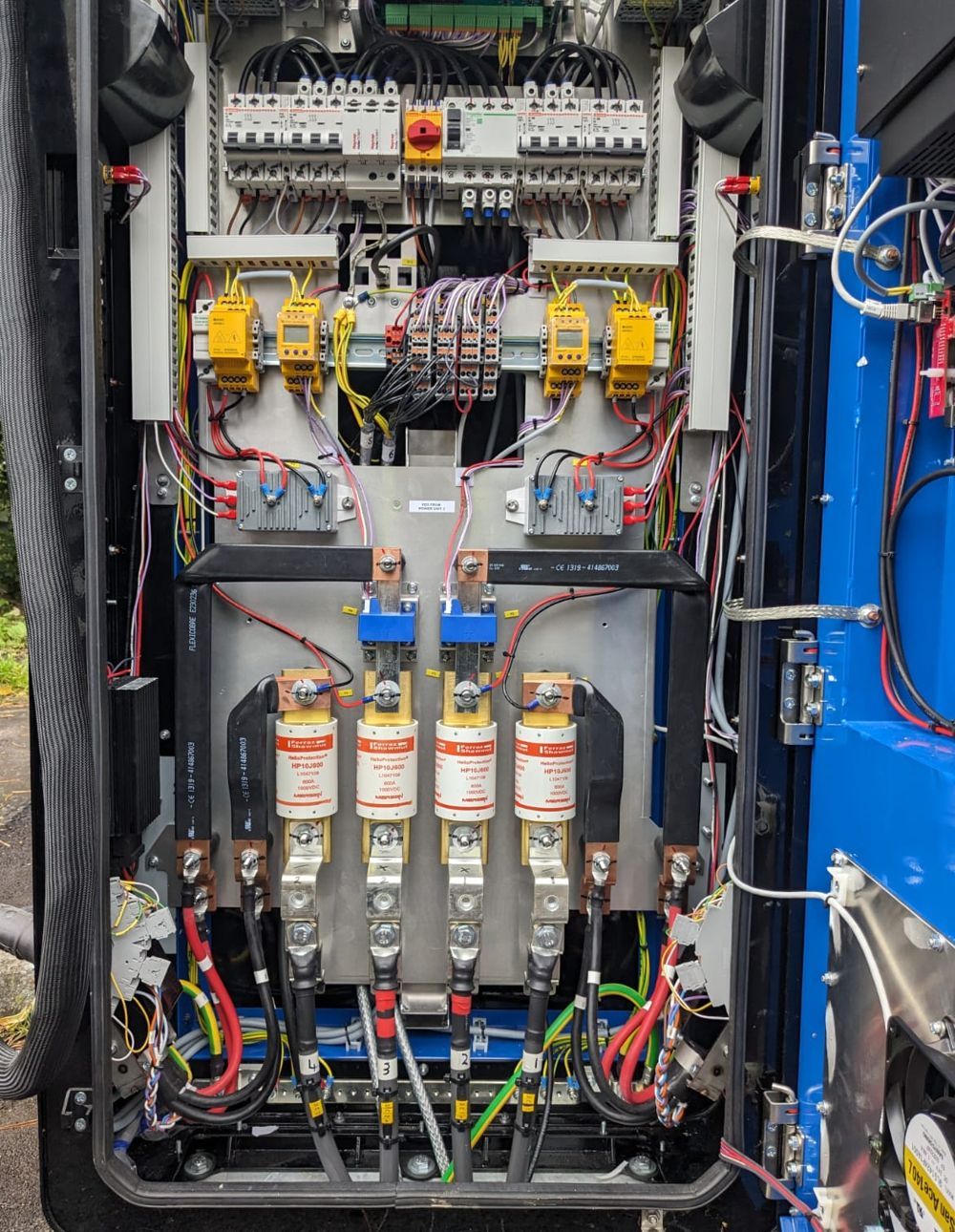 Open electric cabinet with complex wiring, fuses, and circuit breakers.