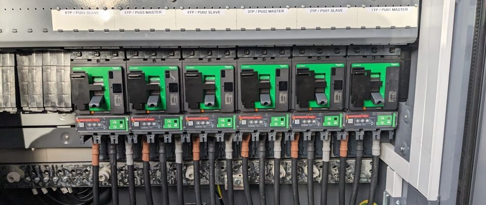 An electrical panel with a row of green and black circuit breakers. Wires are connected below.