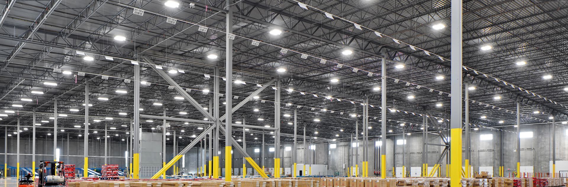 Interior of a large warehouse with many lights on the ceiling. Gray walls and pillars with yellow bases.
