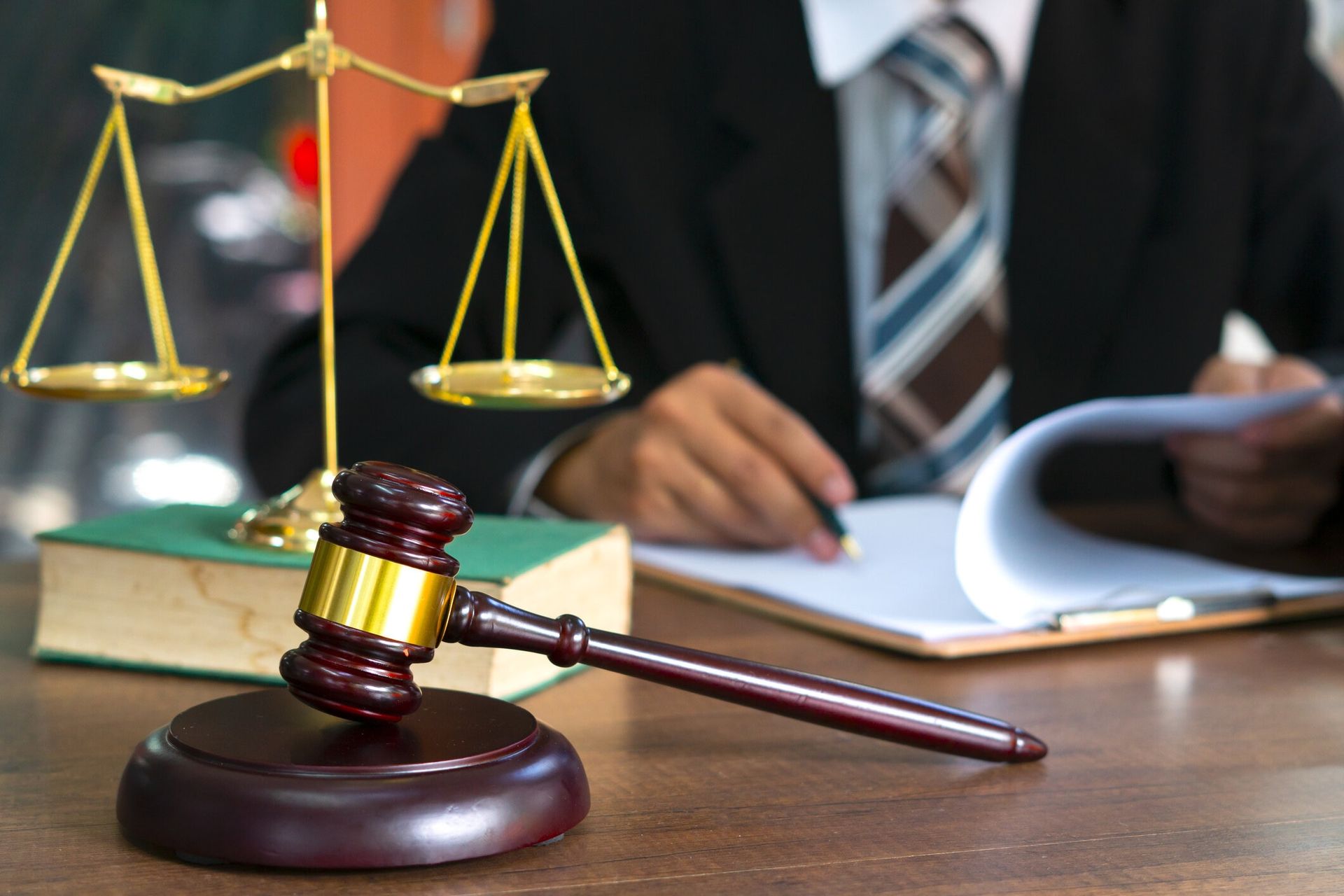 Gavel and scales of justice on a desk with a person in a suit, holding papers.