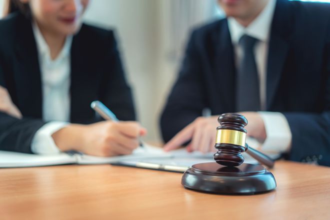 Gavel on table with two people in suits reviewing documents.