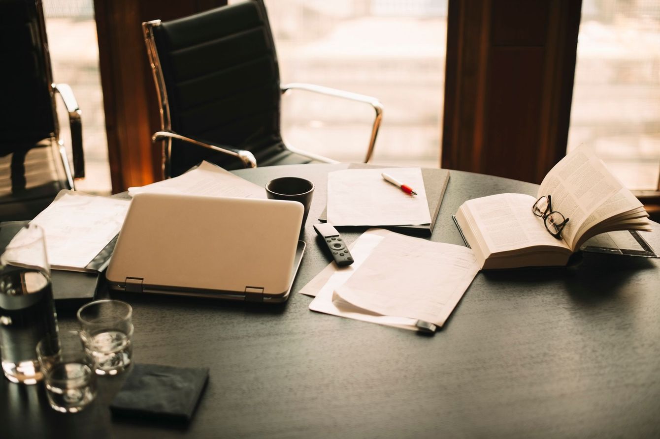 Office desk with laptop, papers, book, glasses, and a water glass.