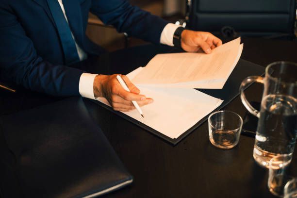 Person in suit writing on paper at a desk, water glasses present.