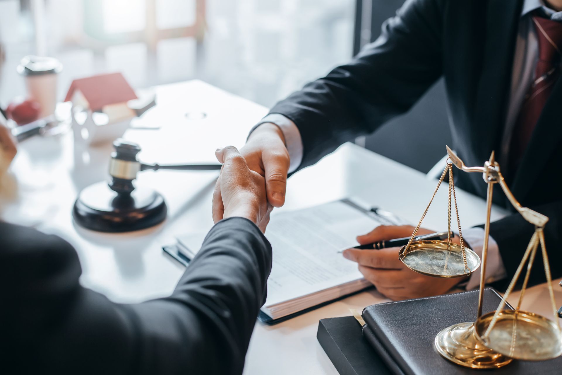 Two people in suits shaking hands at a desk, scales of justice and a gavel are visible.