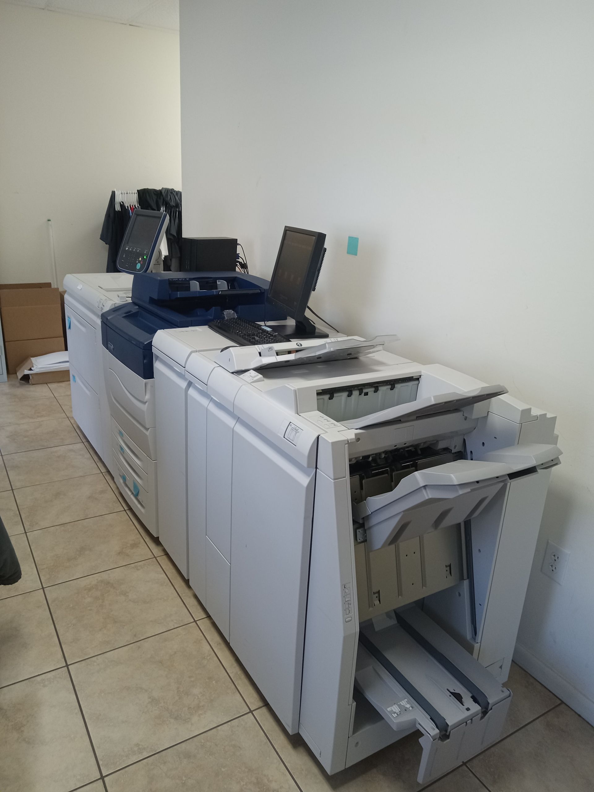A large, white and blue Xerox printer is in a room with a monitor open.