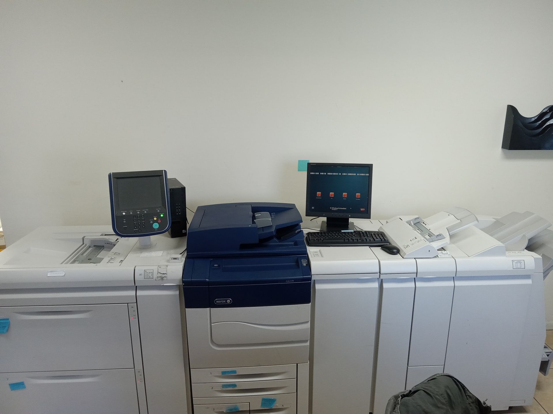 A large printer with a computer setup on a white surface, possibly in an office.