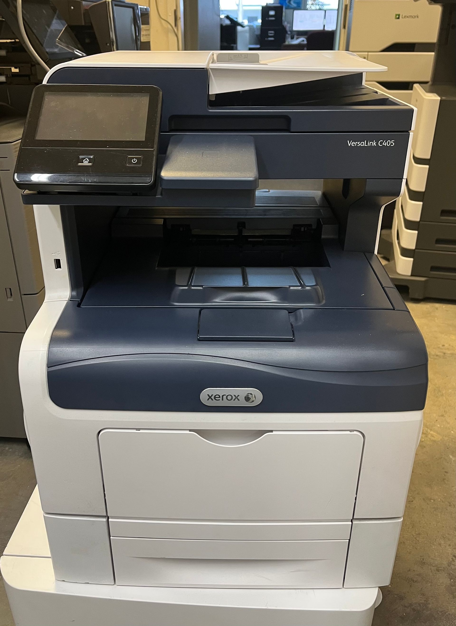 A Xerox multifunction printer, white and dark blue, with a touchscreen, paper trays, and a document feeder.