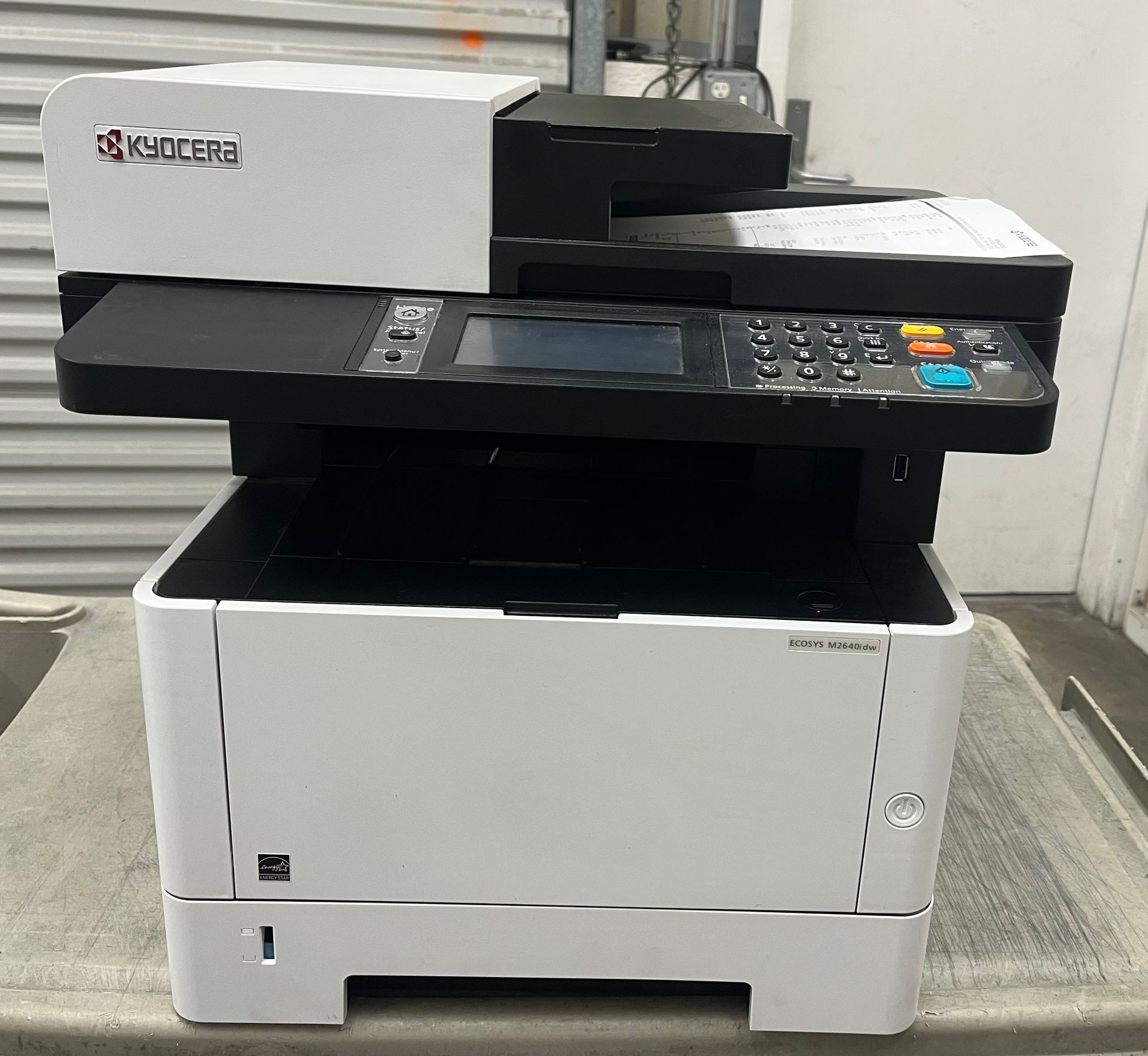 Kyocera multi-function printer with a white body and black top, sitting on a gray surface.