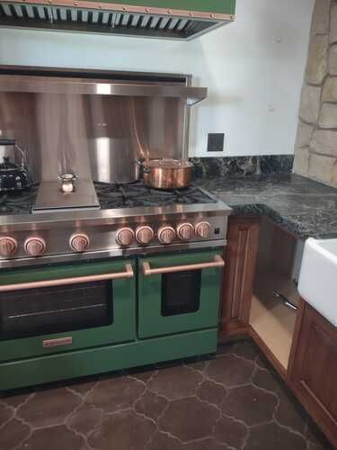 A green stove top oven is sitting in a kitchen next to a sink.