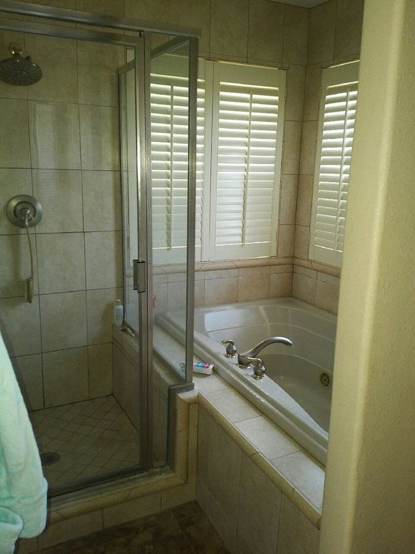 A bathroom with a tub and a shower with shutters on the windows.