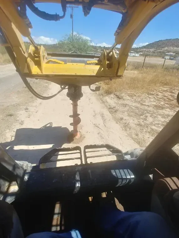 A person operating a yellow auger drilling a hole in the ground outdoors on a sunny day.