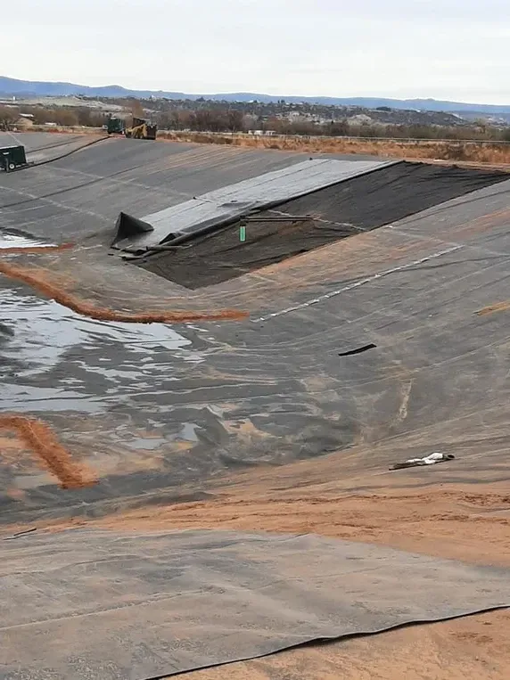 Black plastic-lined basins on a hillside, possibly a landfill or containment area, under a cloudy sky.