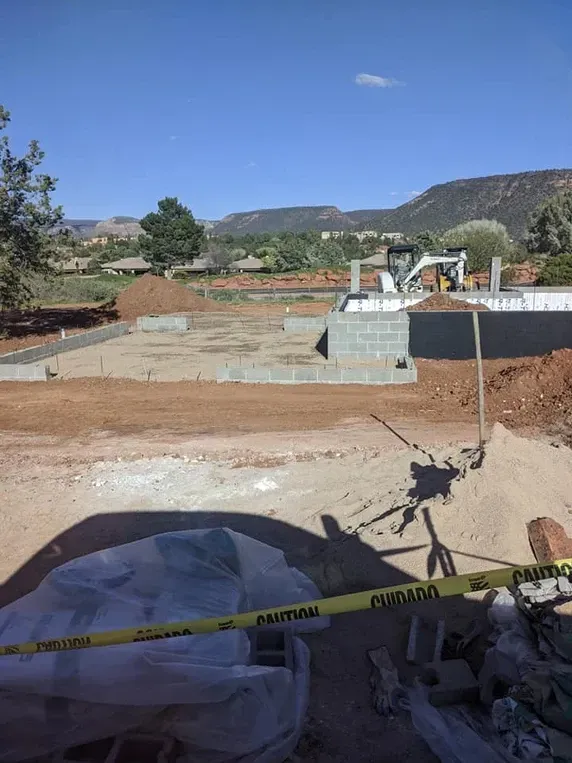Construction site with concrete foundation and backhoe. Mountains in background, sunny day.