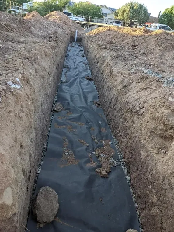A long trench dug in brown soil, lined with black fabric; a construction site.