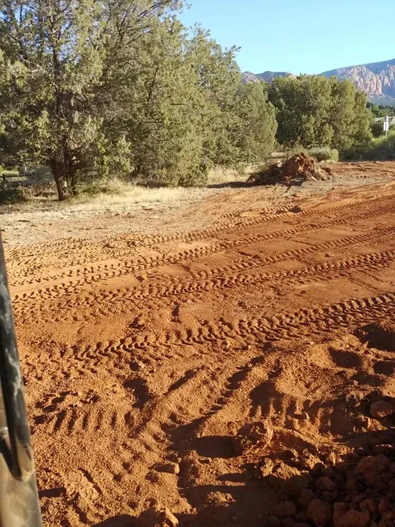 Red dirt field with tractor tracks, small dirt pile, trees in background.