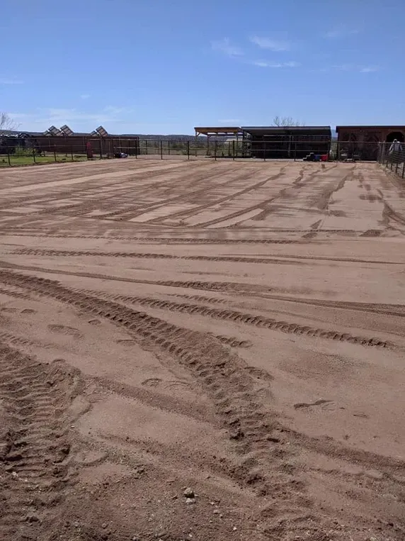 Dirt field with tire tracks under a blue sky, buildings in the background.