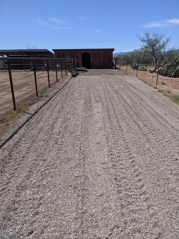 A gravel driveway leads to a brick building with an arched entrance on a sunny day.