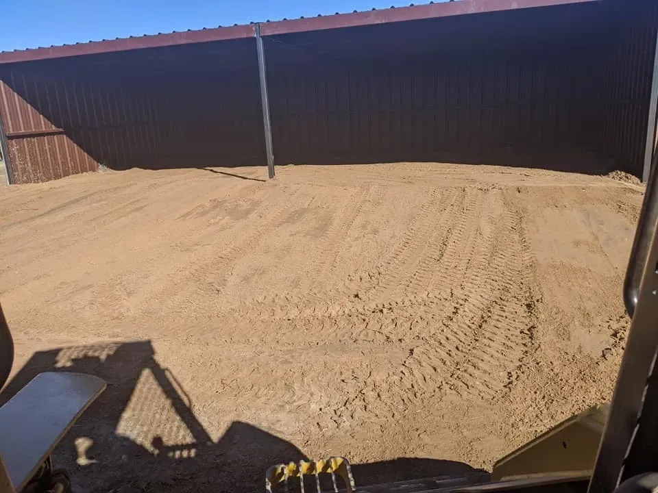 A sandy area under a metal roof, likely a work space. A skid steer's bucket is visible in the foreground.