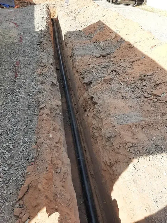 Black pipe in a narrow trench dug in the dirt, likely for utilities.