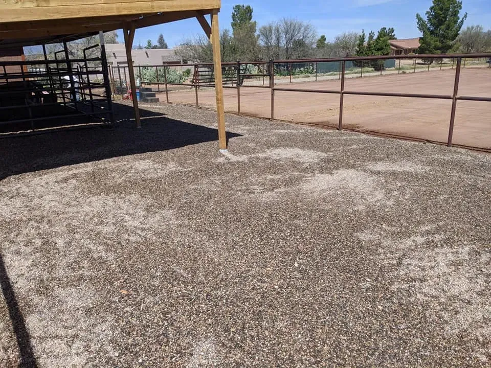 Gravel-covered area next to a wooden-framed structure and brown metal fence under a blue sky.