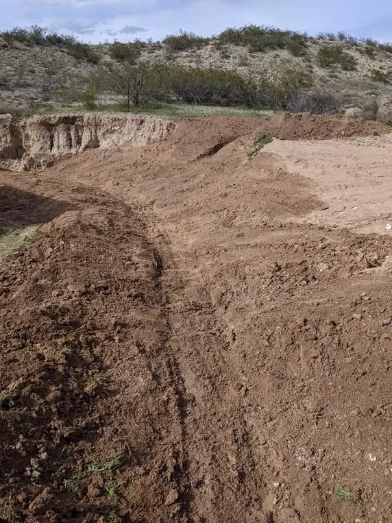 Dirt terrain with excavated areas and hillside in background.