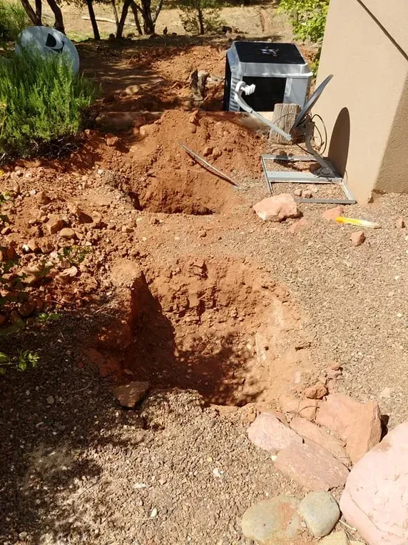 Holes dug in red dirt near a building and equipment.