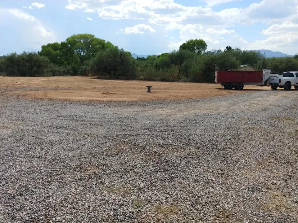 Gravel lot with trailer and truck, trees and sky in the background.