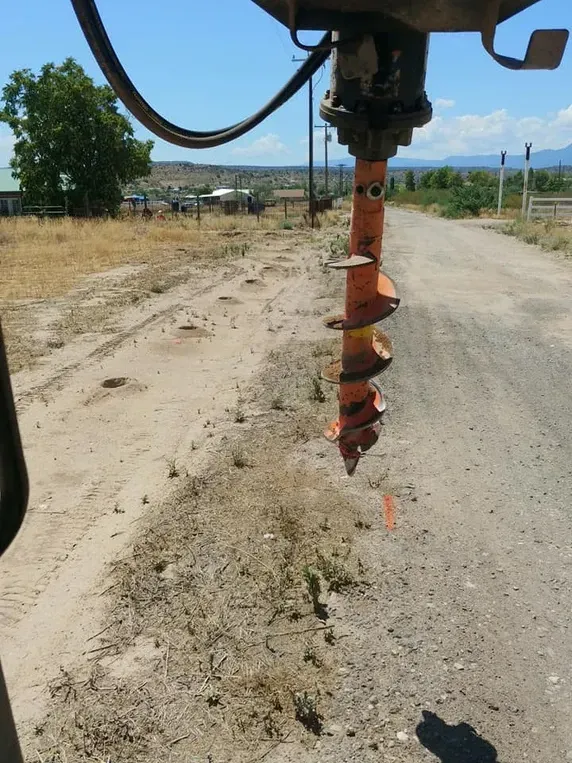 An orange auger drill, on a dirt road, drilling a hole.