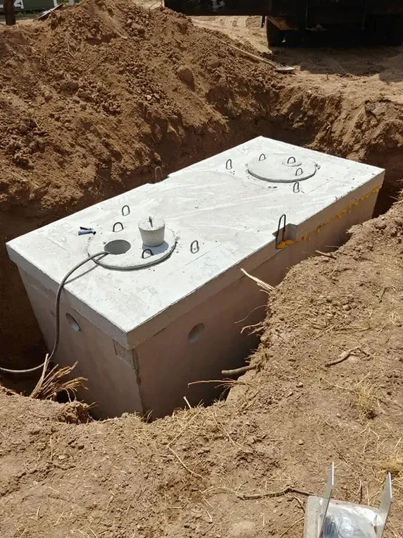 Concrete septic tank in an excavated trench, with access covers visible.