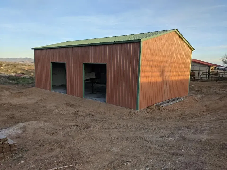 Brown metal shed with green trim and roof; two open bays; built on dirt.
