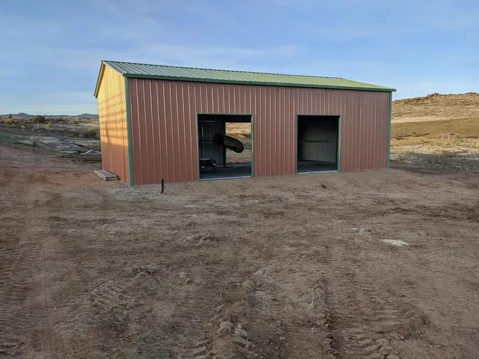 Brown metal shed with two openings, set in a dry, open landscape under a blue sky.