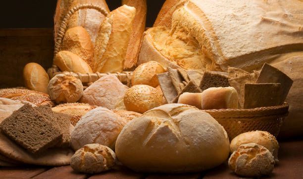 Variety of freshly baked breads on a wooden table; light and dark crusts, different shapes and textures.