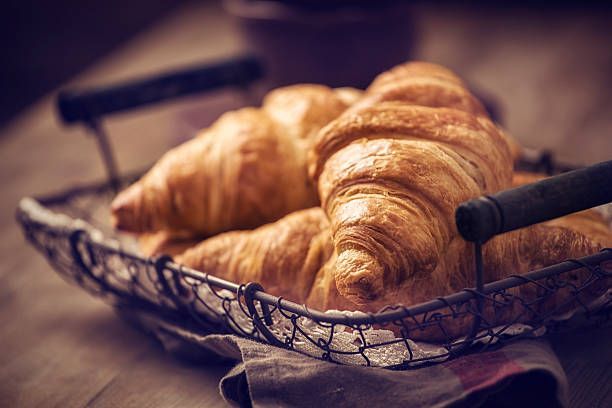 Fresh croissants in a wire basket on a wooden surface, lit from the side.