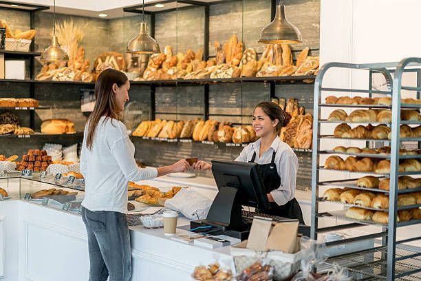 Woman buying pastry at a bakery counter; the baker smiles, with various breads displayed.
