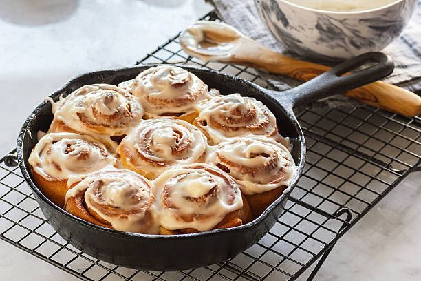 Cinnamon rolls in a cast iron skillet, drizzled with white icing, sitting on a cooling rack.