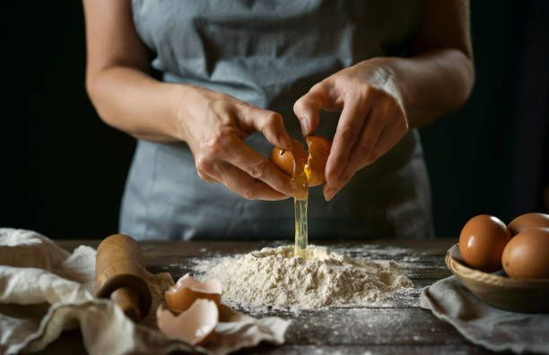 Woman cracking an egg into flour on a wooden table, preparing to bake.