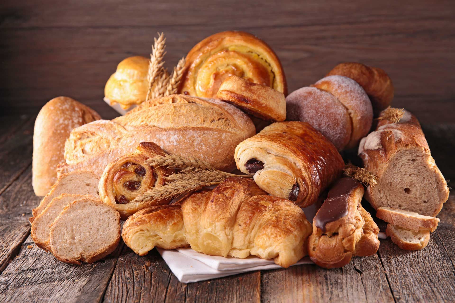 Assortment of baked goods on a wooden surface, including bread, pastries, and croissants.
