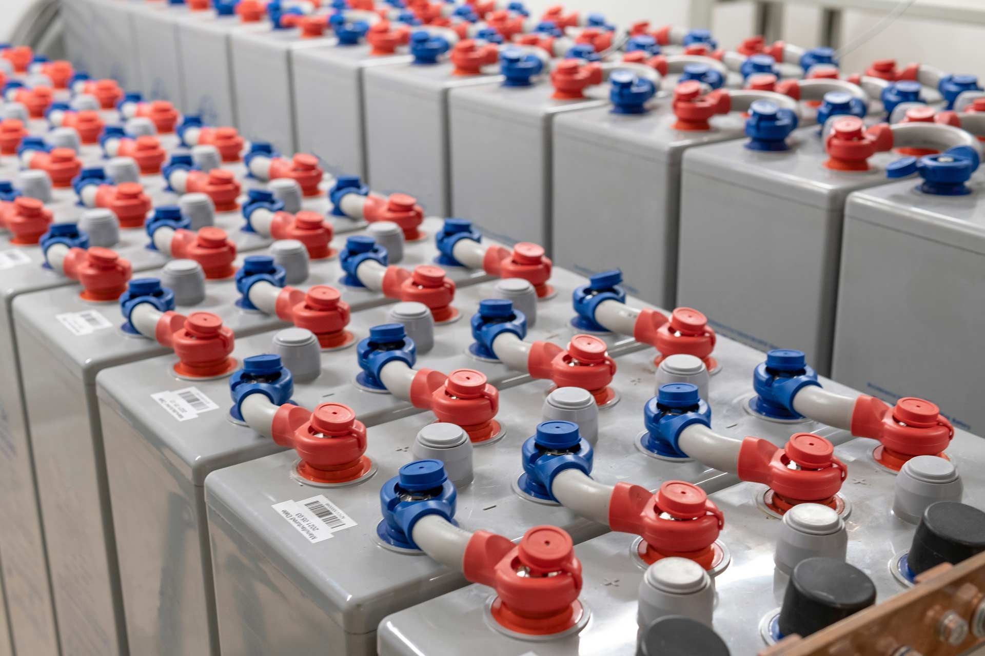 Rows of industrial batteries with red and blue ventilation caps.