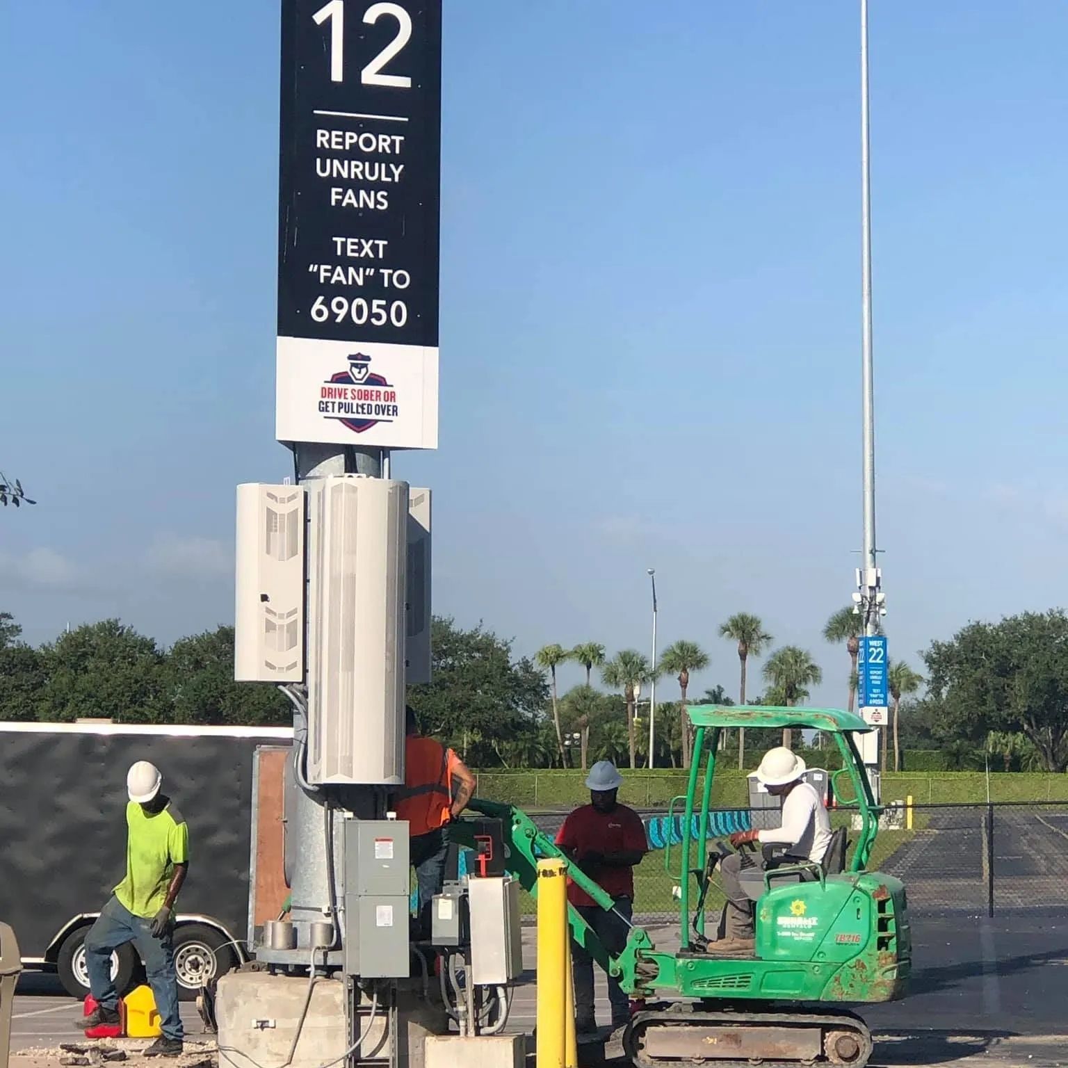 Workers installing a communications tower near a sign that reads