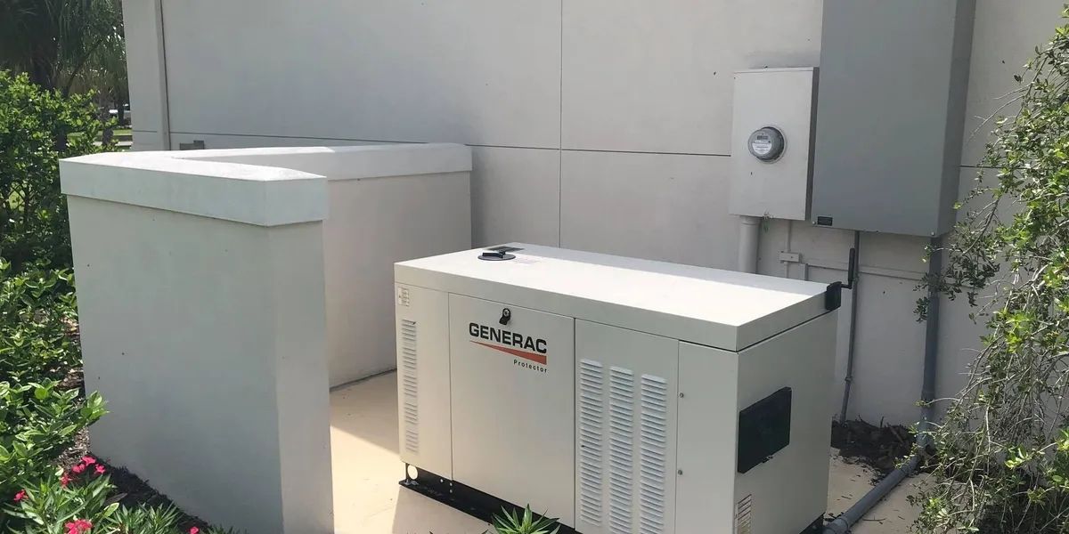 A white generator and an adjacent unit sit outside next to some electrical boxes and greenery.