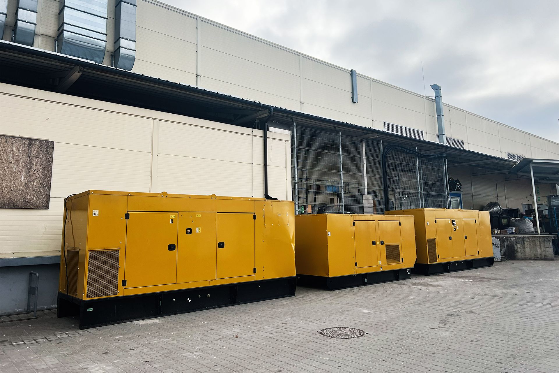 Three yellow generators stand in a row in front of a large warehouse building.