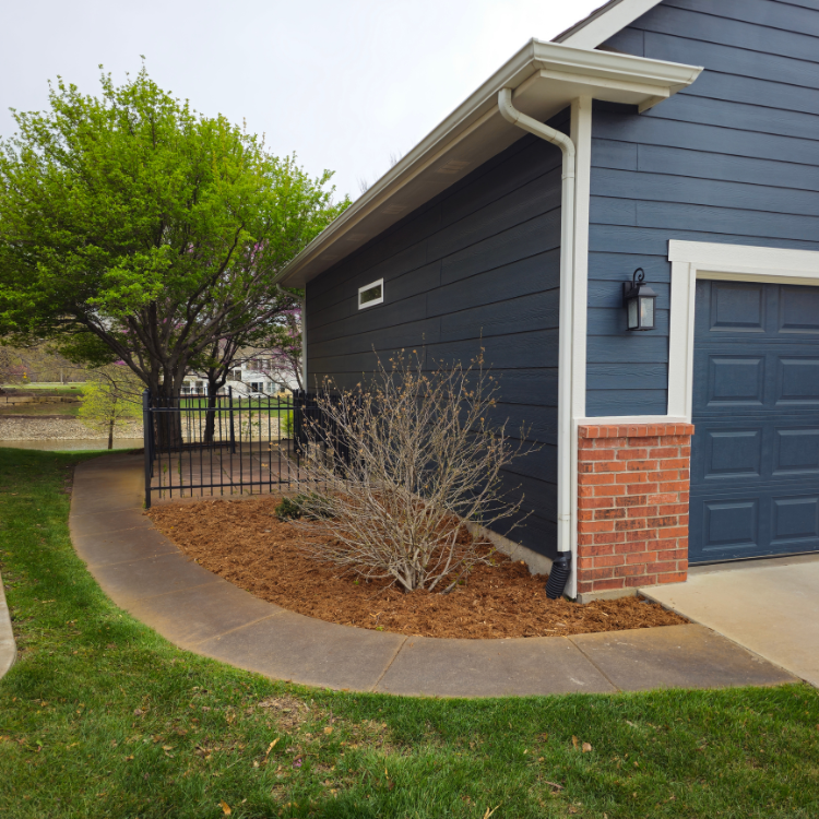 Blue house with brick column, curved concrete path, and mulch-covered planting bed.