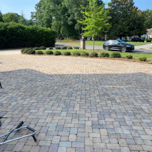 Paver driveway with a small circular garden, a car, and green trees.