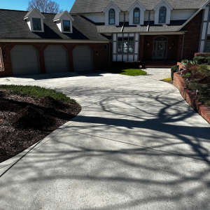 Driveway leading to a two-story house with a brick facade and three-car garage; large tree shadow.